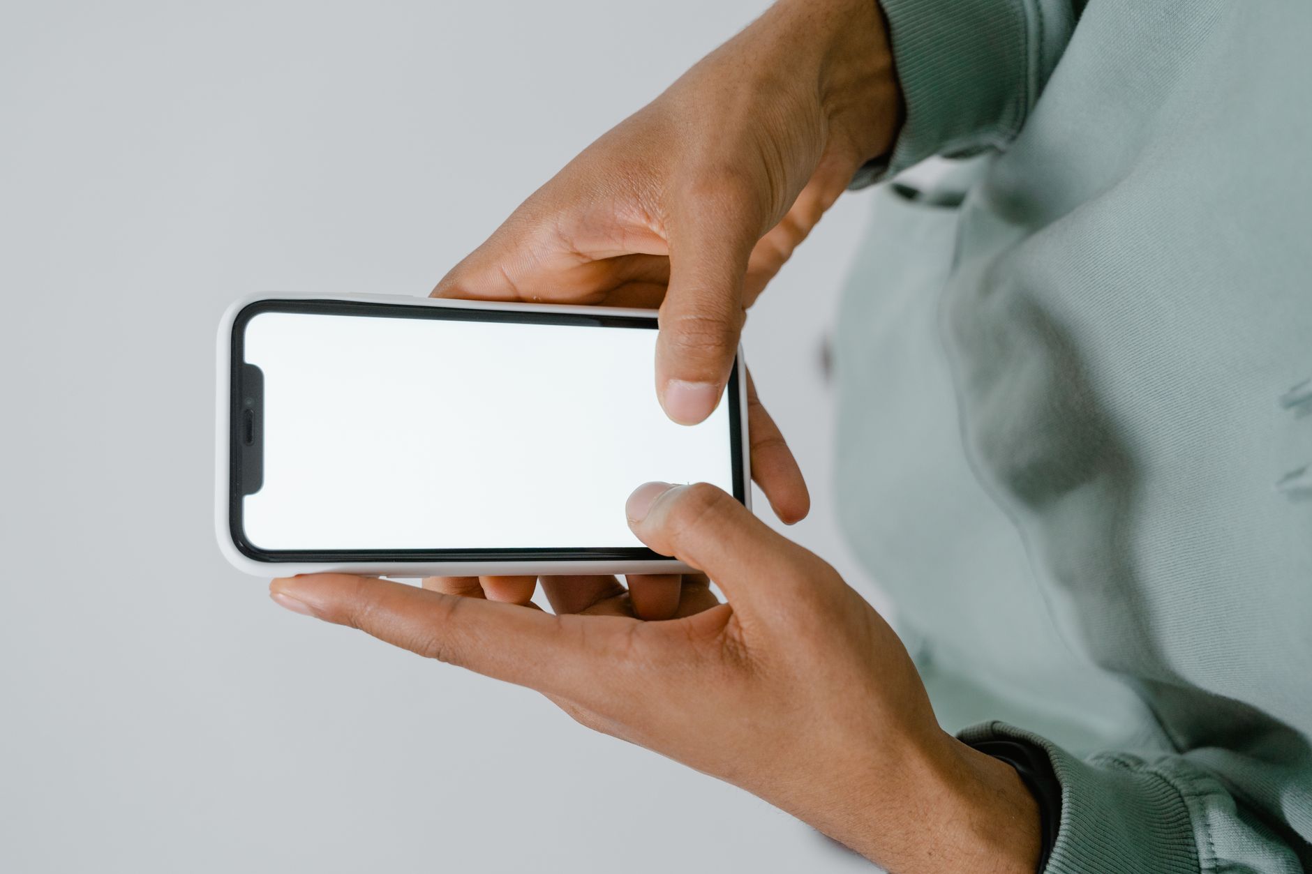 Due mani tengono in orizzontale uno smartphone con lo schermo bianco