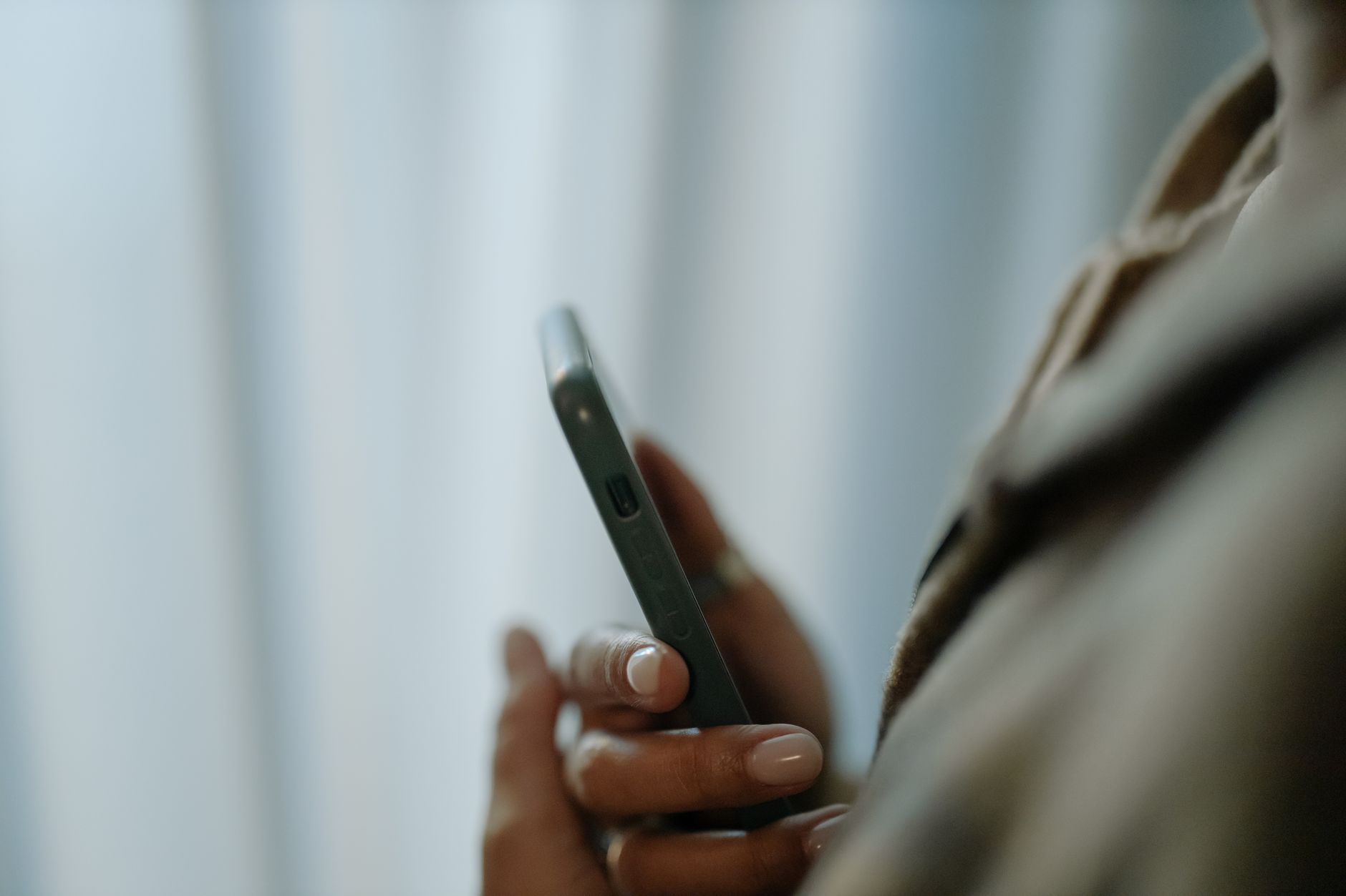 Una mano regge uno smartphone in una stanza in penombra, con tende chiare sullo sfondo