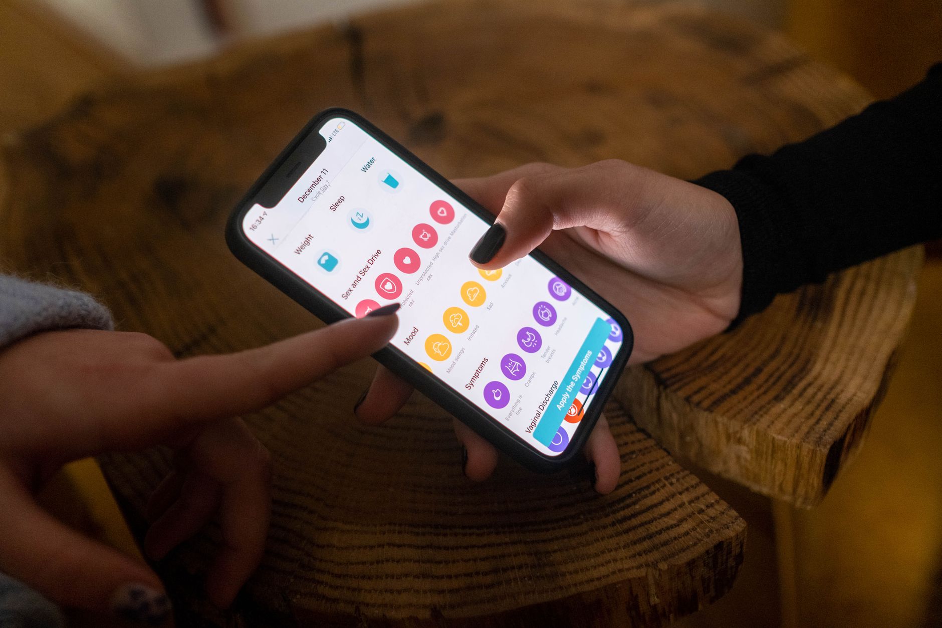 Due persone toccano insieme lo schermo di uno smartphone appoggiato su un tavolo di legno